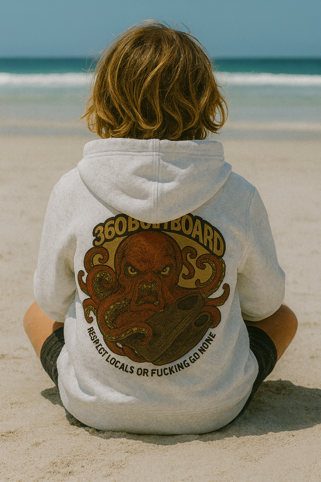 Pessoa sentada na praia, vestindo um moletom com estampa de polvo. Oceano ao fundo.