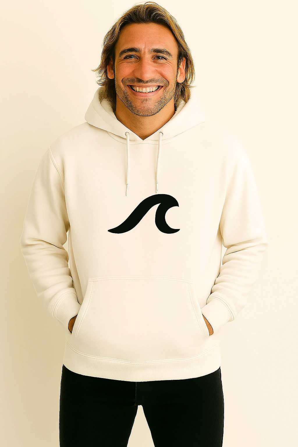 Homem com capuz creme e logotipo de onda preta sorri, com as mãos nos bolsos.