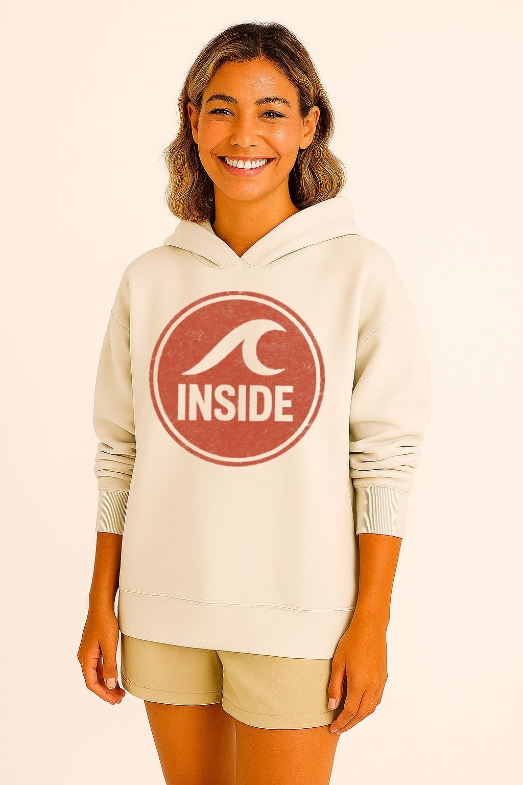 Mulher vestindo um moletom creme com um logotipo circular vermelho com um desenho de onda e a palavra "INSIDE".