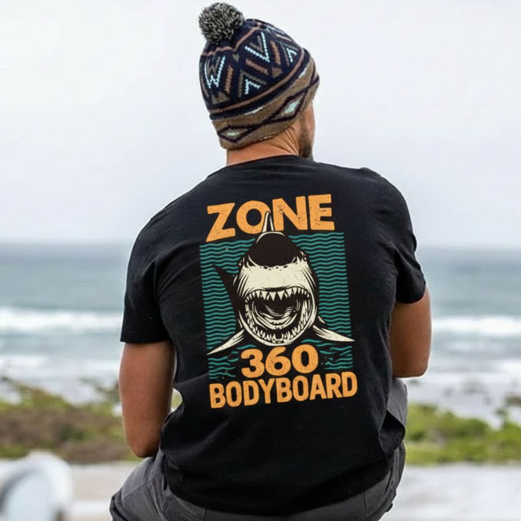 Pessoa vestindo uma camiseta preta da Zone 360 ​​e um gorro com estampa de tubarão, olhando para o oceano.
