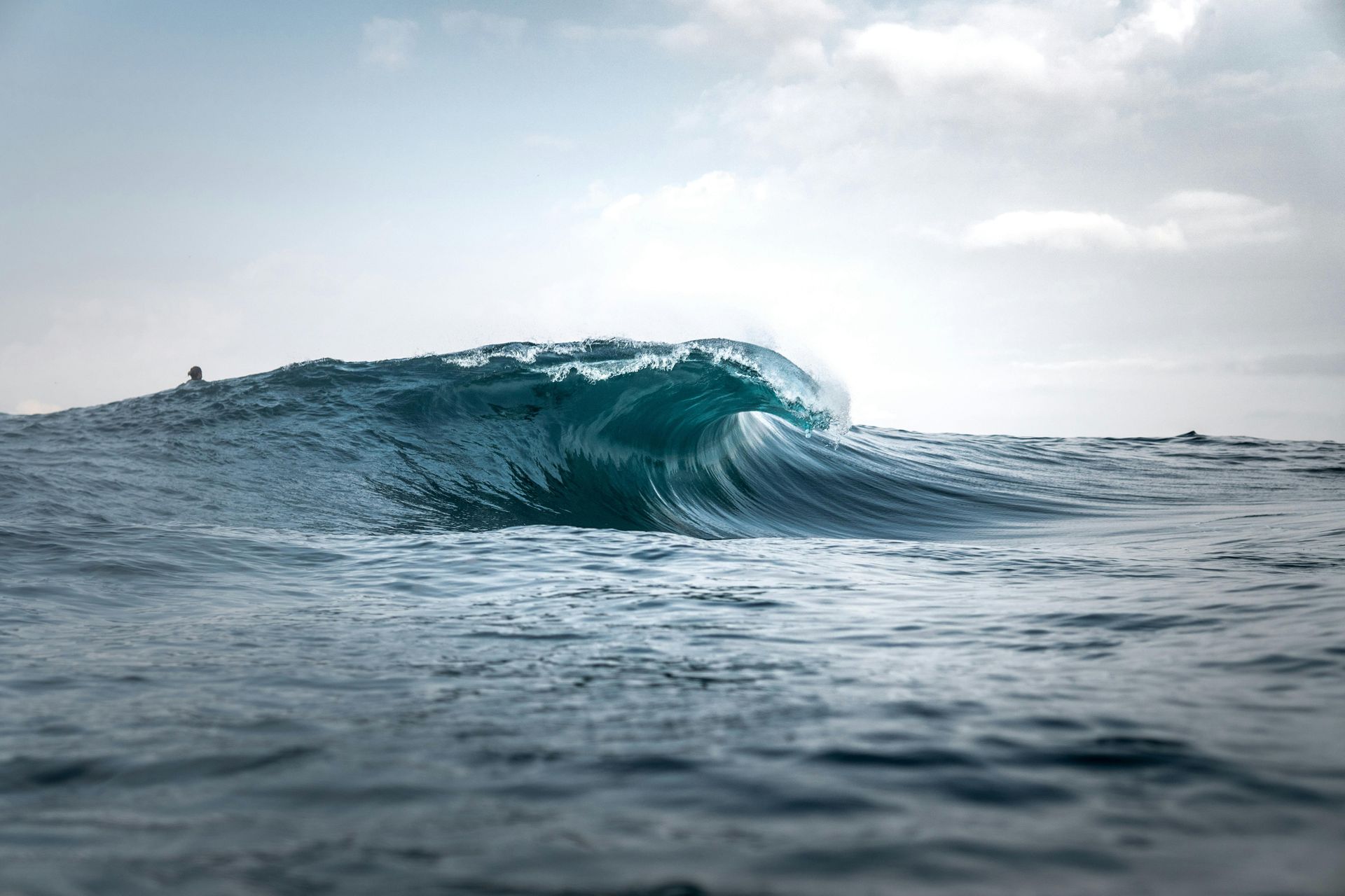 Ondas do oceano se formando, água azul-turquesa quebrando no mar, céu nublado.