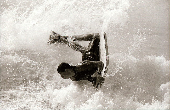 Pessoa praticando bodyboard em águas turbulentas e brancas.
