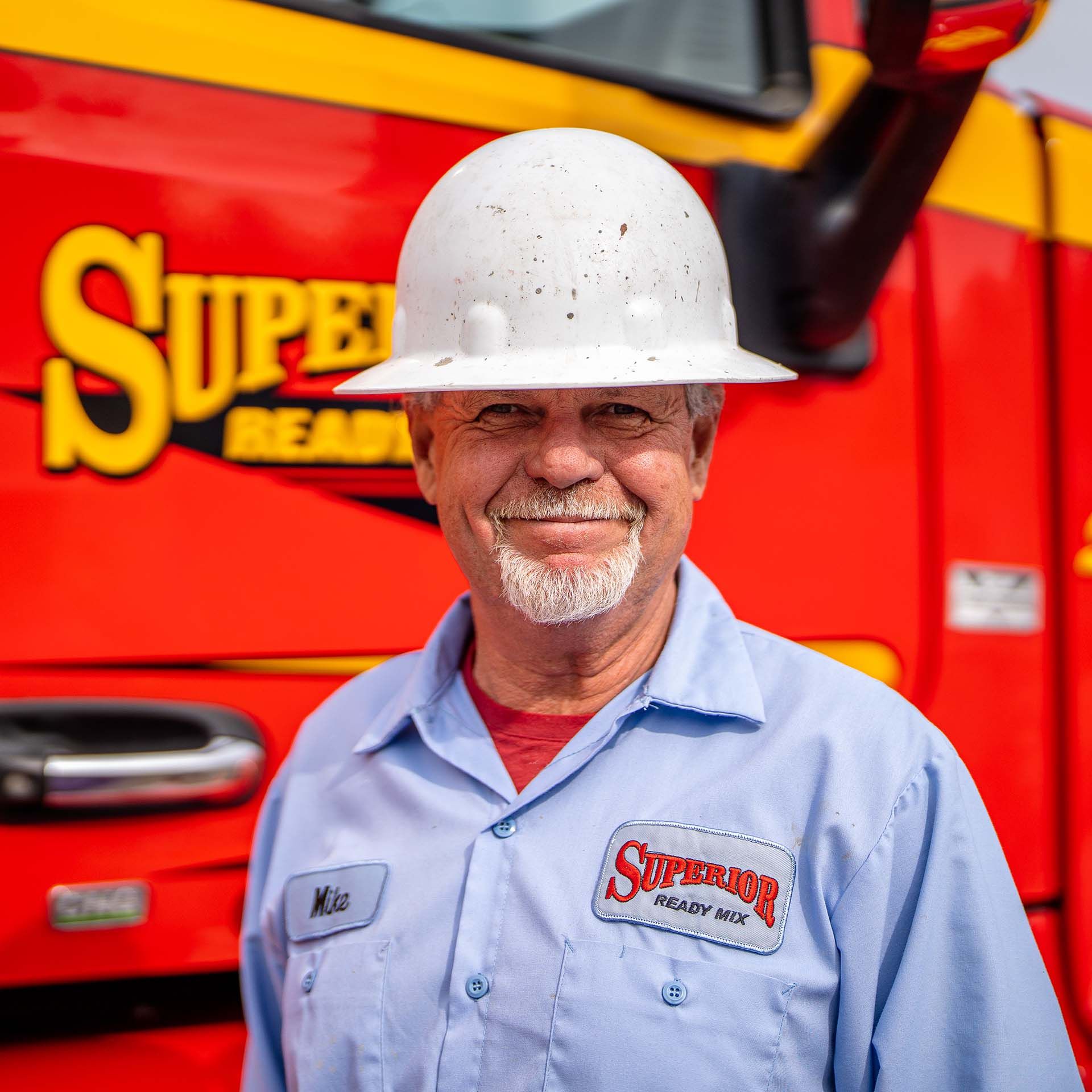 A man wearing a hard hat is standing in front of a red truck.