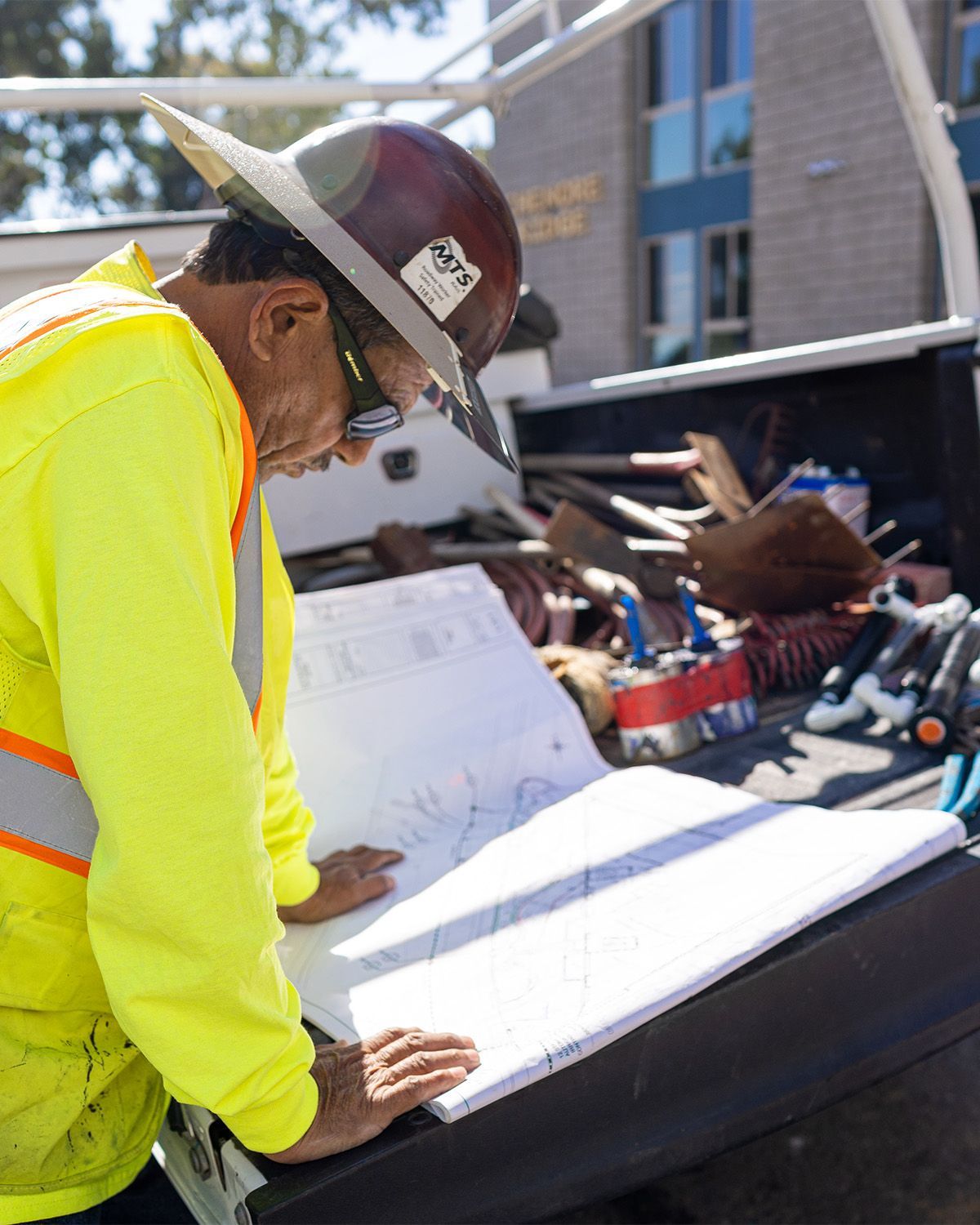 A man wearing a hard hat is looking at a blueprint