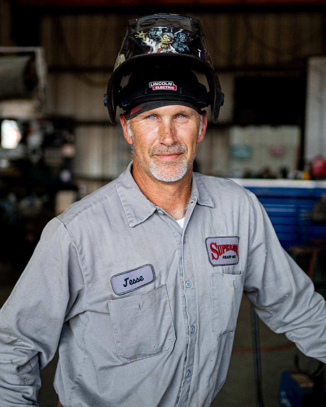A man wearing a welding helmet is standing in a garage.