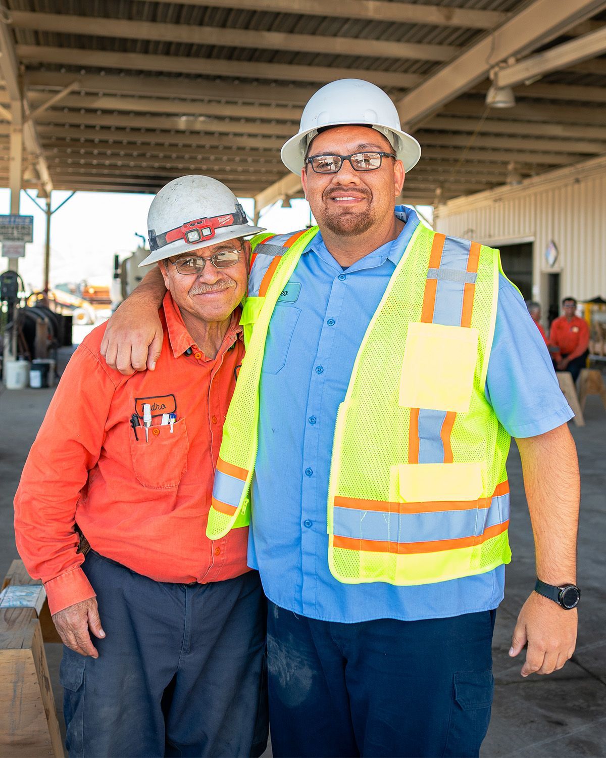 Two men wearing hard hats and safety vests are posing for a picture.