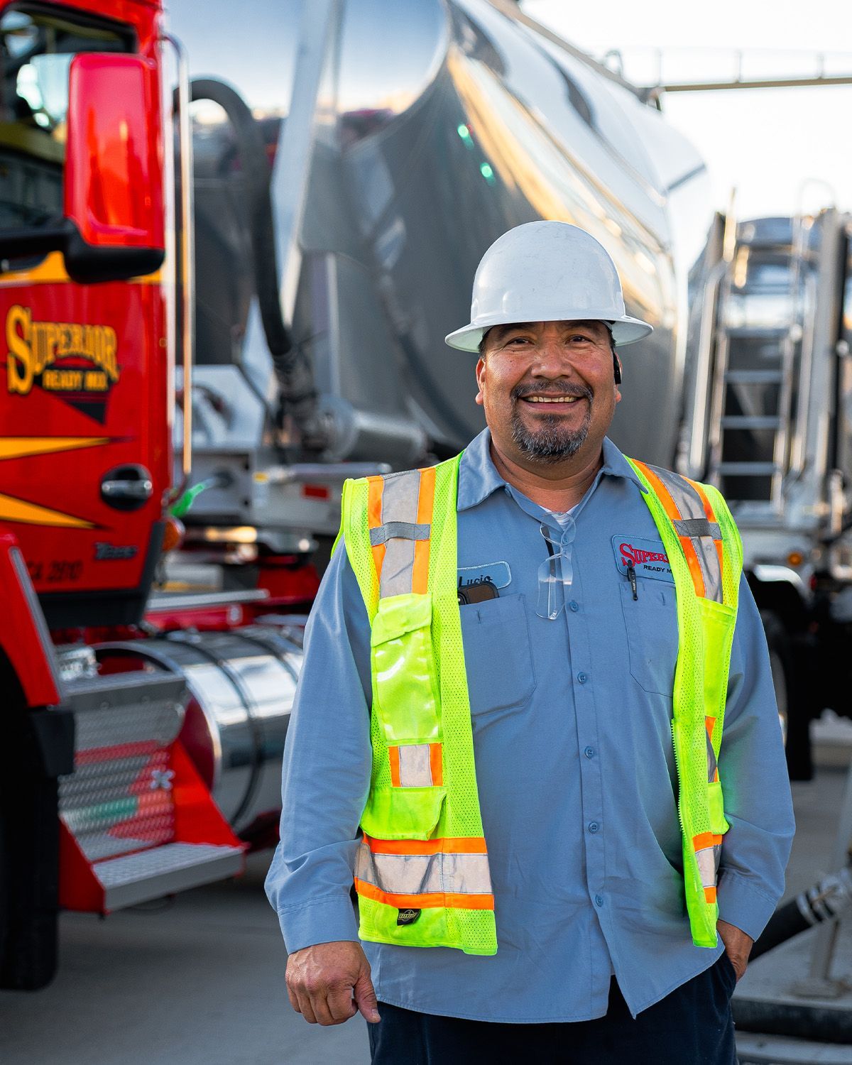 A man wearing a hard hat and safety vest is standing in front of a truck.