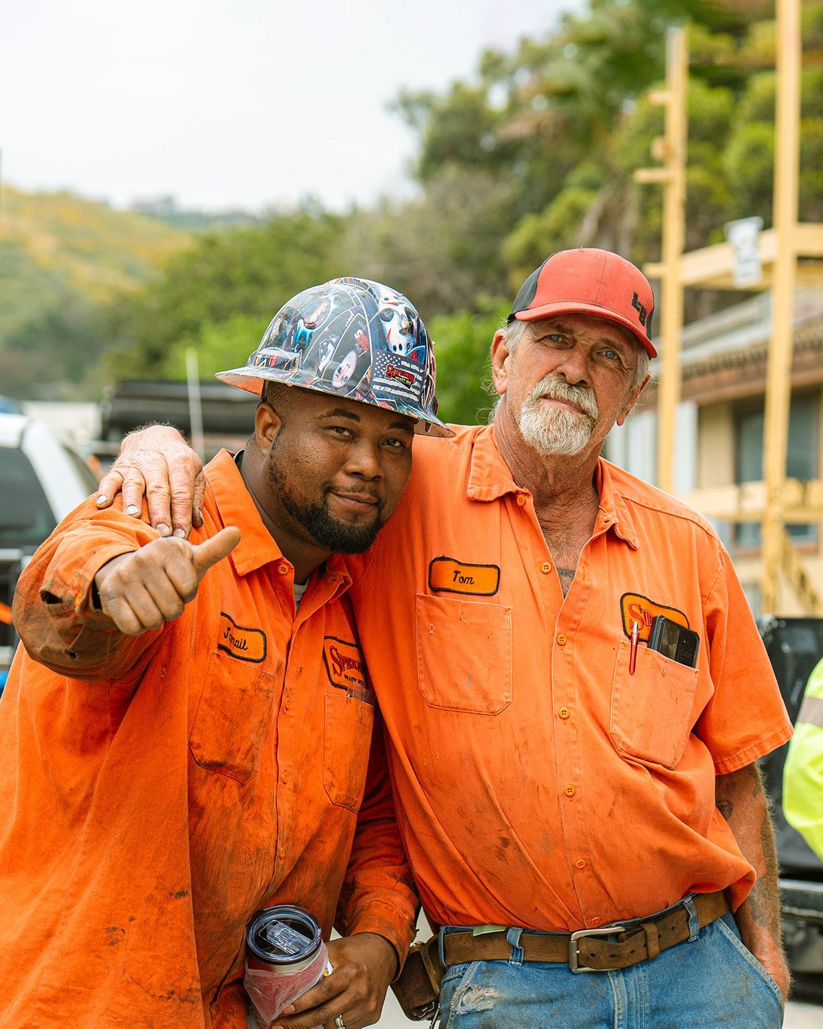 Two construction workers are posing for a picture and one of them is wearing a hard hat.