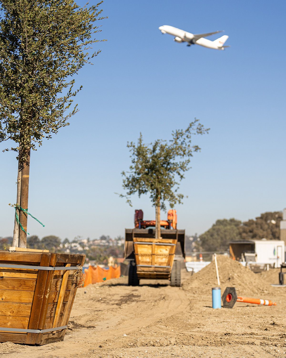 A plane is flying over a construction site with a tree in the foreground
