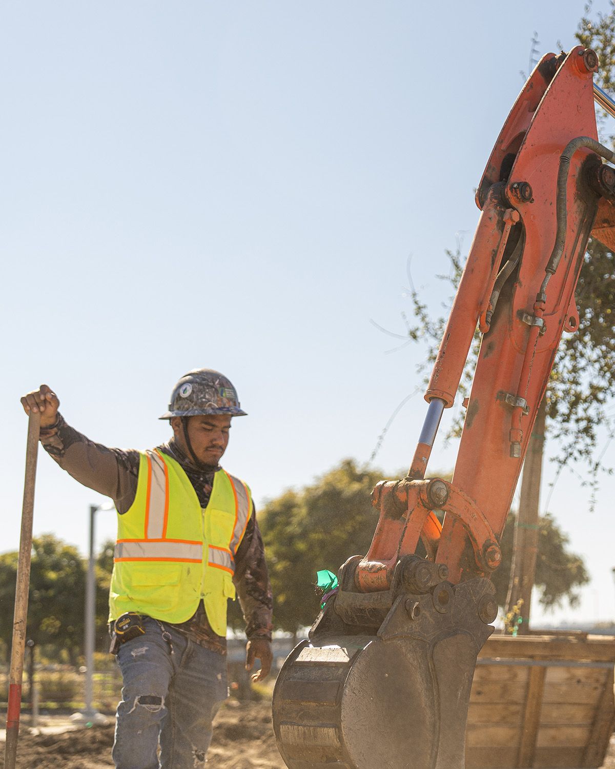 A construction worker is standing in front of an excavator holding a shovel.