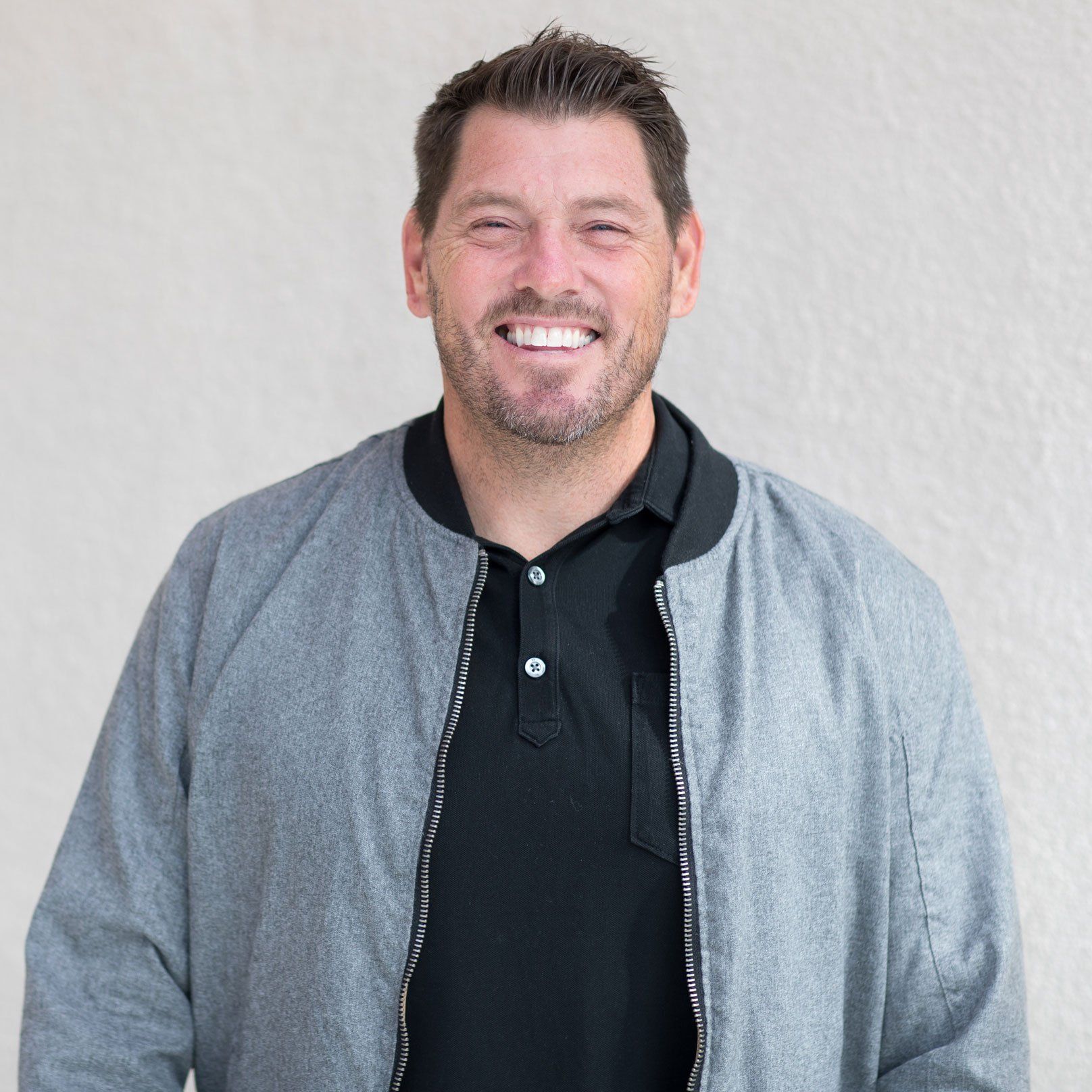 A man wearing a grey jacket and a black shirt is smiling