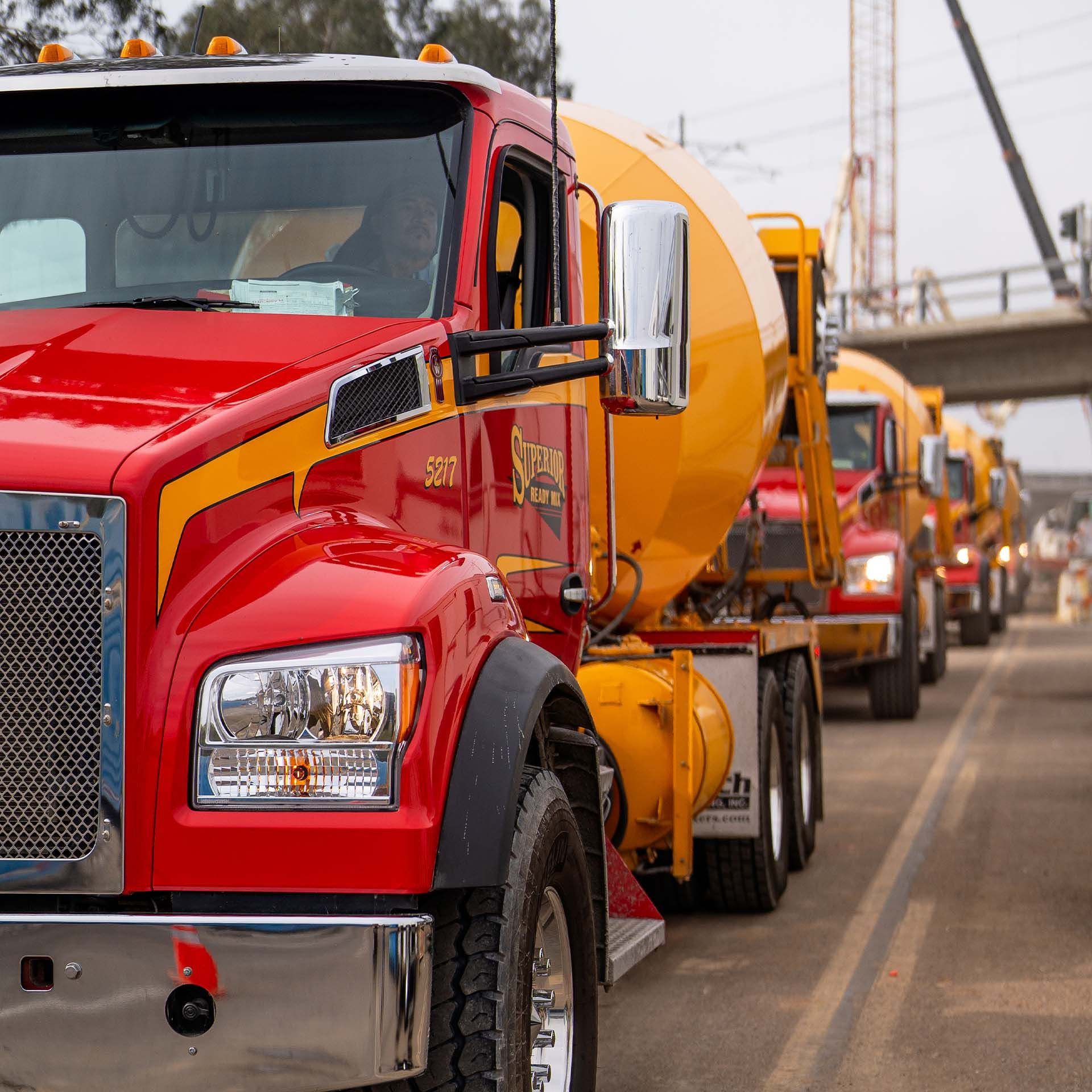 A row of red and yellow trucks are driving down a road