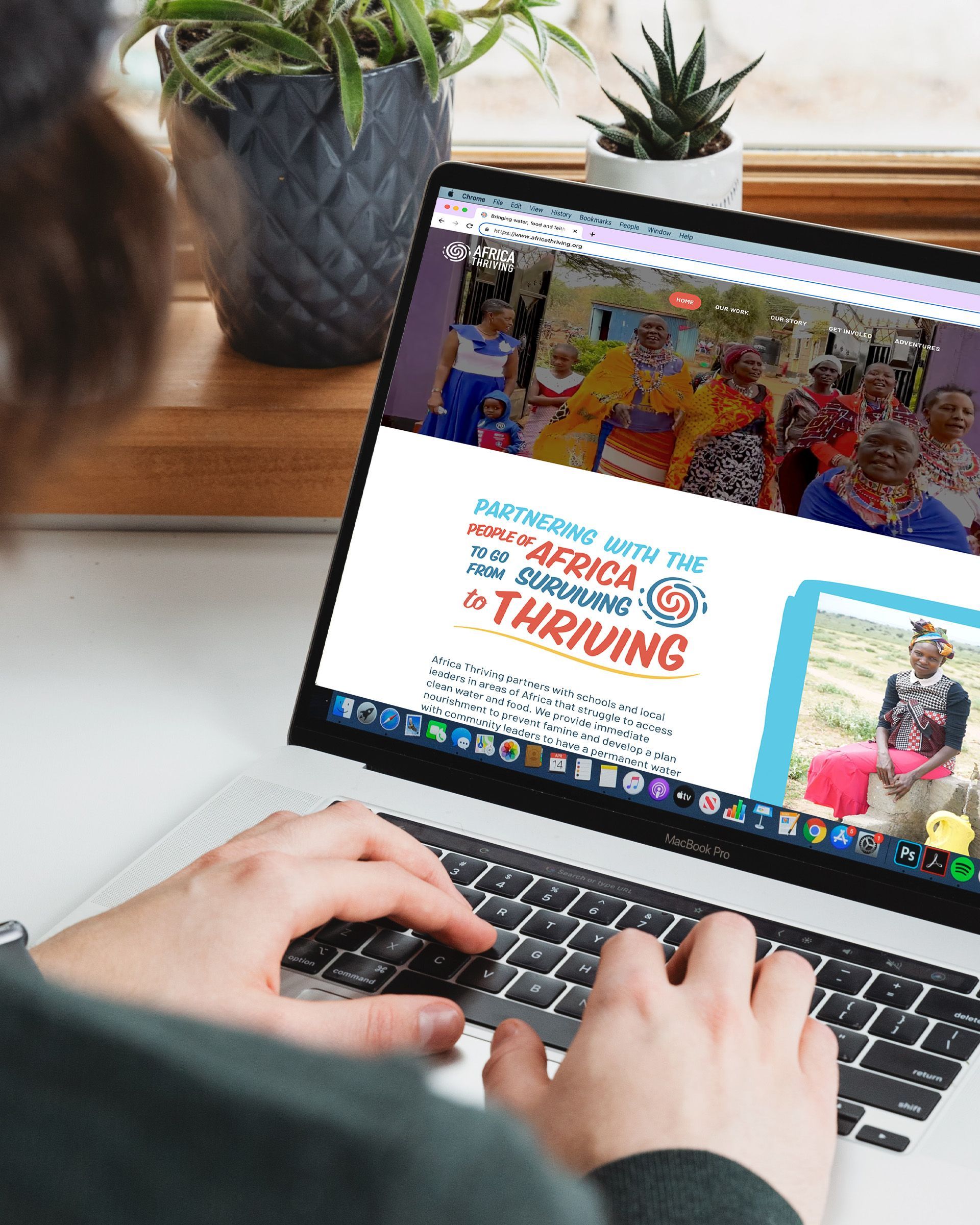 A person is typing on a laptop computer showing the Africa Thriving website.