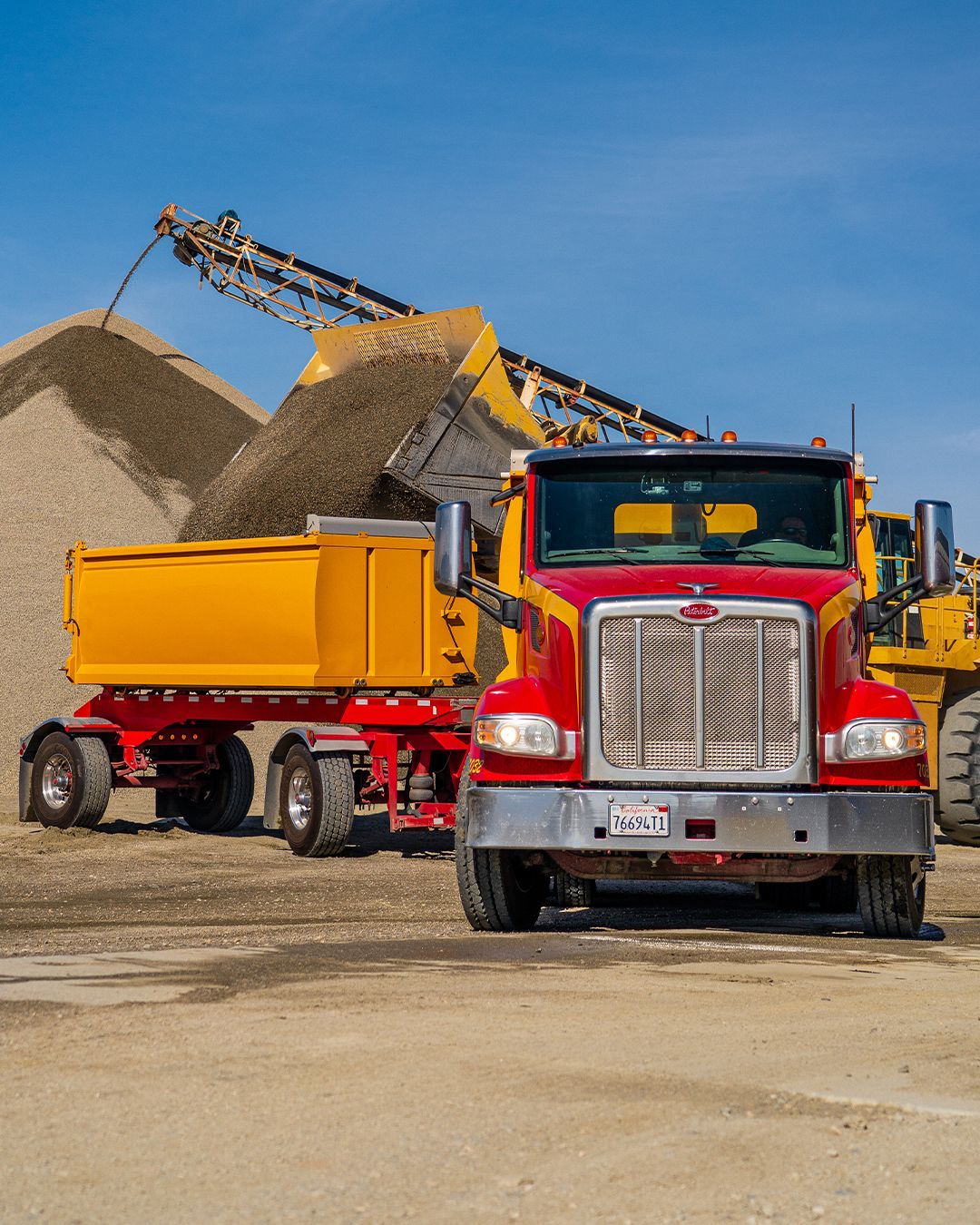 A dump truck is being loaded with gravel by a bulldozer.