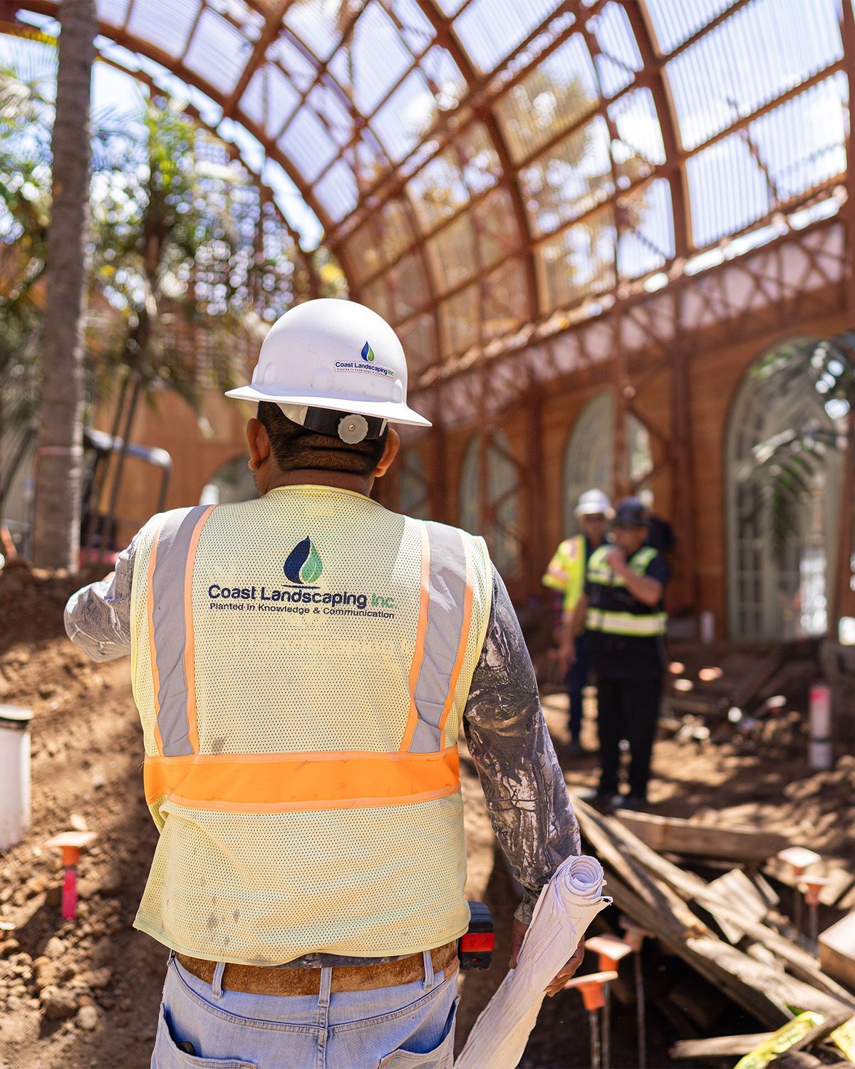 A construction worker wearing a hard hat and safety vest is standing in front of a building under construction.