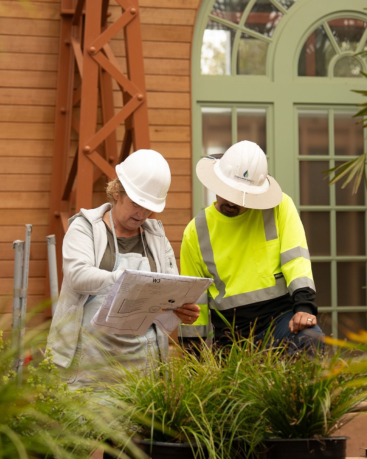 A man and a woman wearing hard hats are looking at a piece of paper