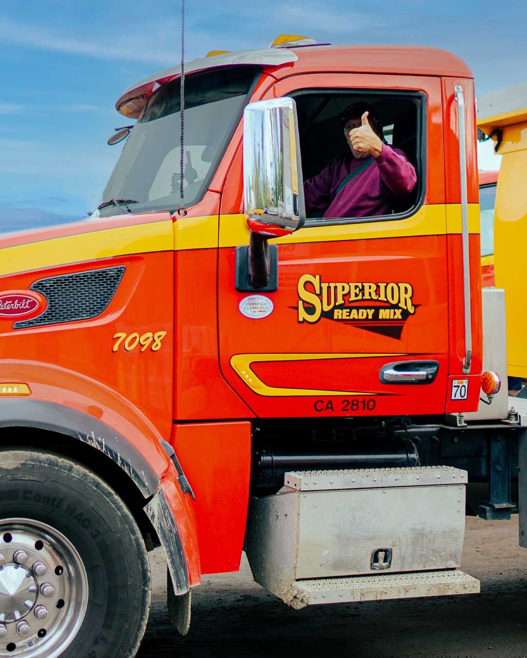 A man is giving a thumbs up in the driver 's seat of a superior ready mix truck