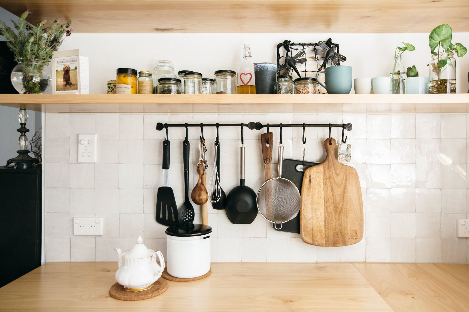 A Meticulously Organized Kitchen Features Light Wood Shelving, White Tile Backsplash, And A Hanging Rack Displaying Various Cooking Utensils — Concept Kitchens In Port Macquarie, NSW