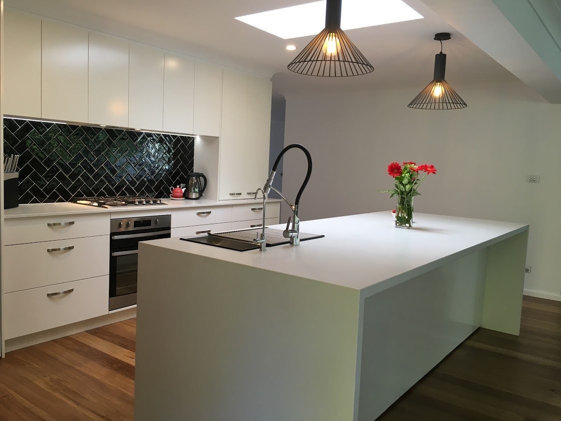A kitchen with white cabinets and a large island with a vase of flowers on it. — Concept Kitchens In Port Macquarie, NSW