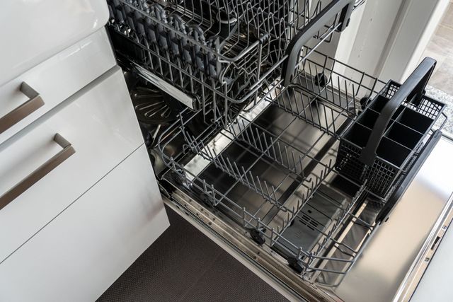 Open dishwasher with clean dishes in a kitchen beside white cabinets