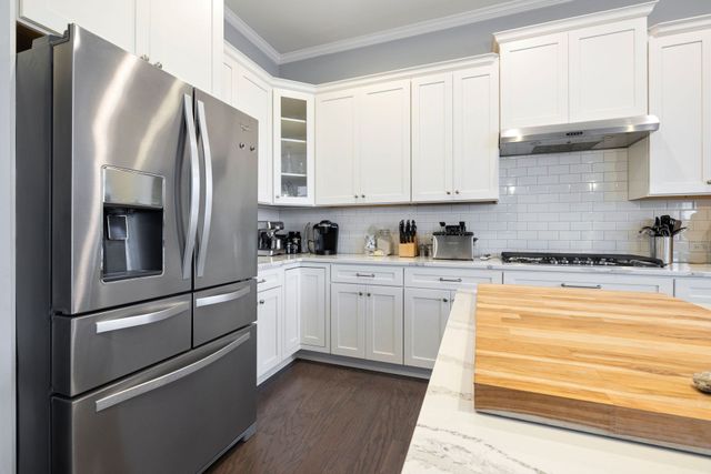Modern white kitchen with stainless steel fridge, white cabinets, gray backsplash, and wooden island countertop