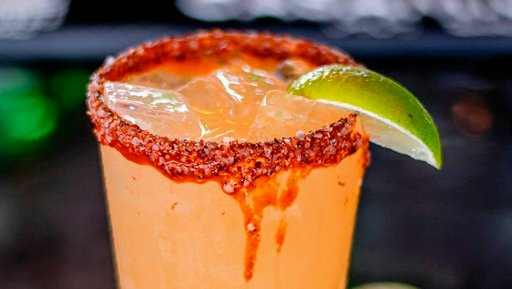 A close up of a margarita with a lime wedge on a table.