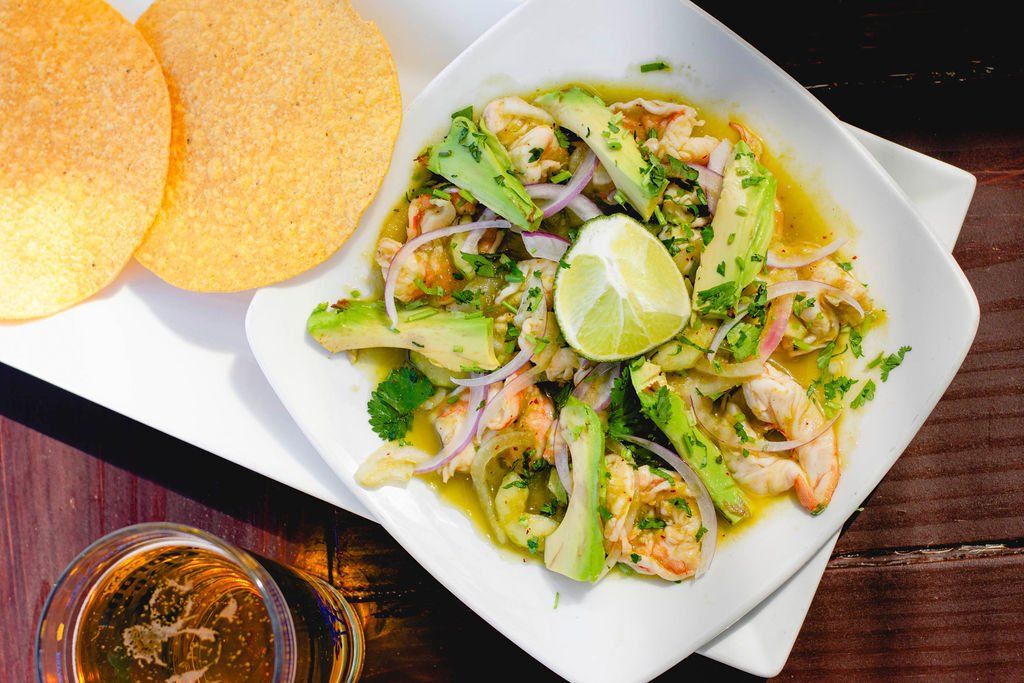 A plate of food with shrimp and avocado on a wooden table.