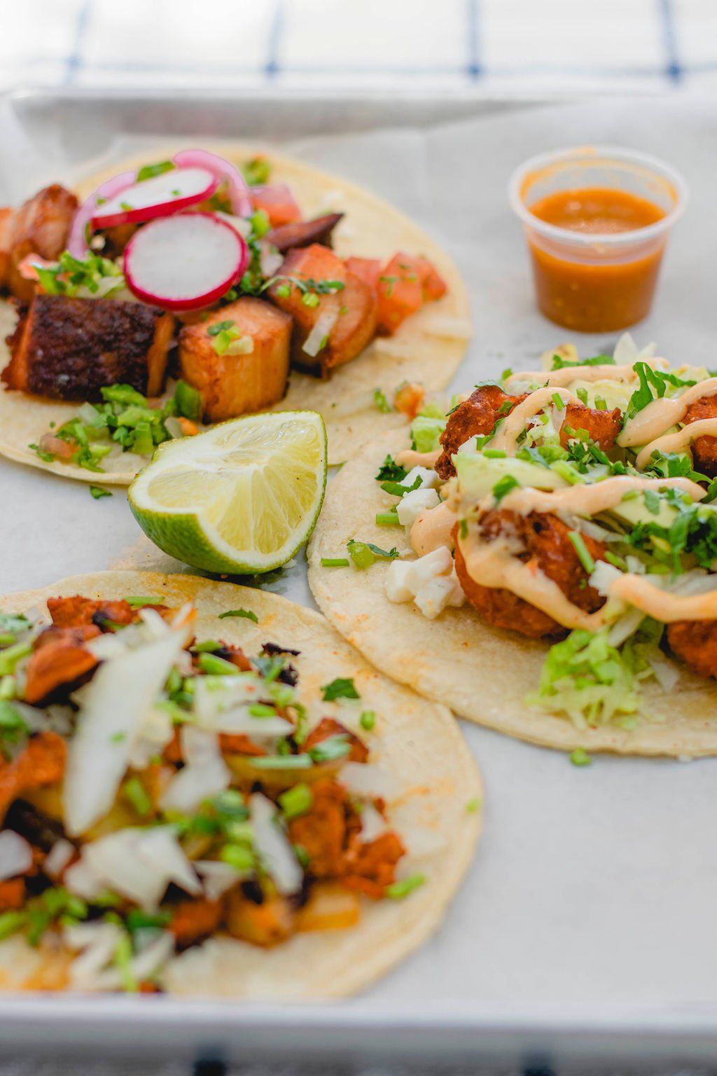 Three tacos are sitting on a white plate on a table.