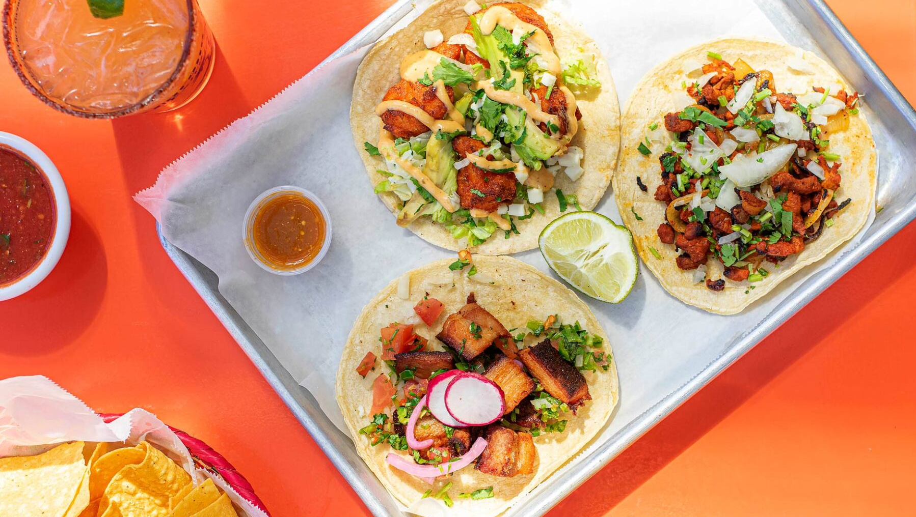 A tray of tacos and chips on an orange table.