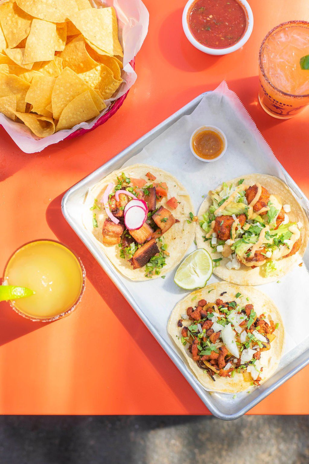 A tray of tacos , chips , and a drink on a table.
