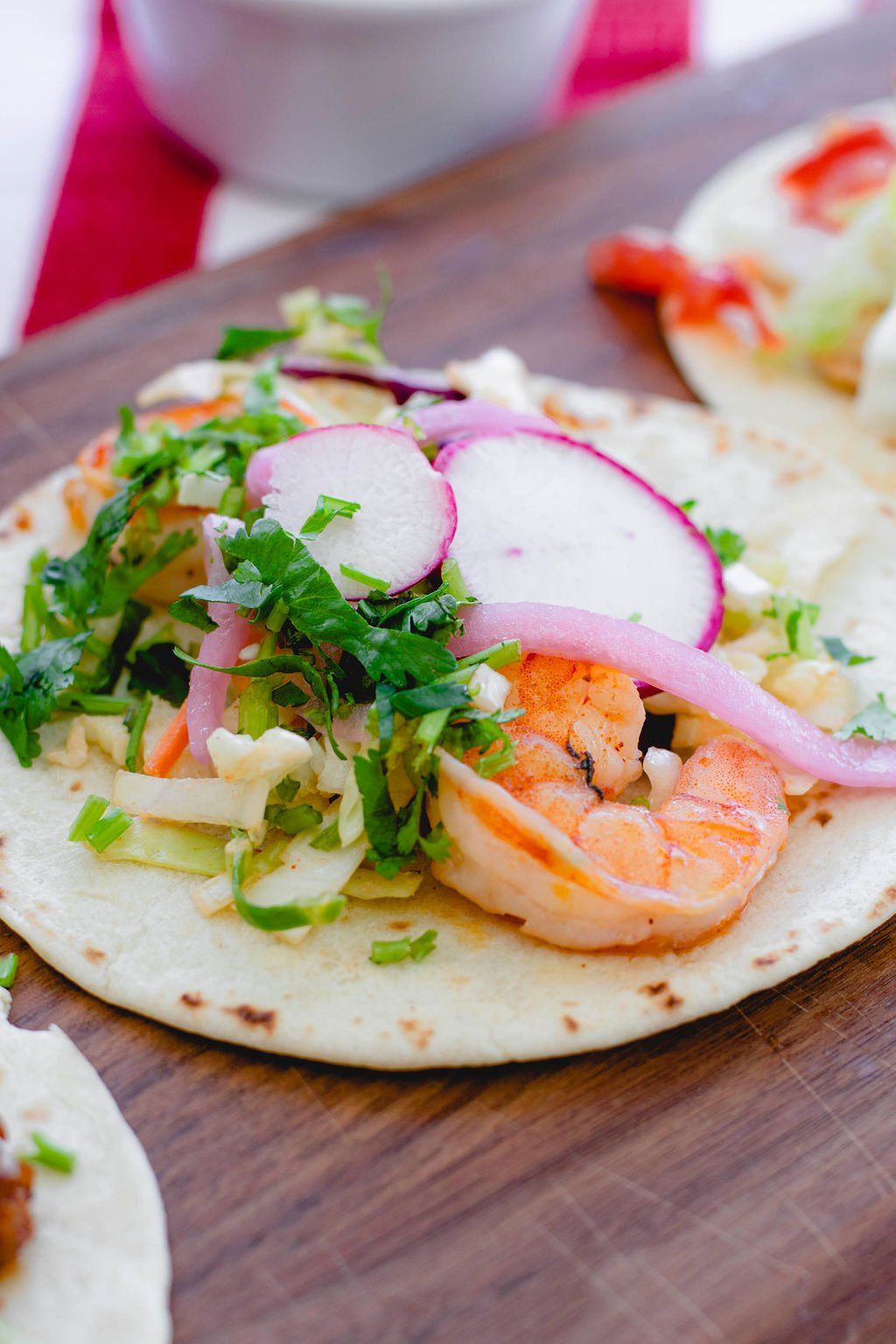 A close up of a taco with shrimp , radishes and onions on a wooden cutting board.