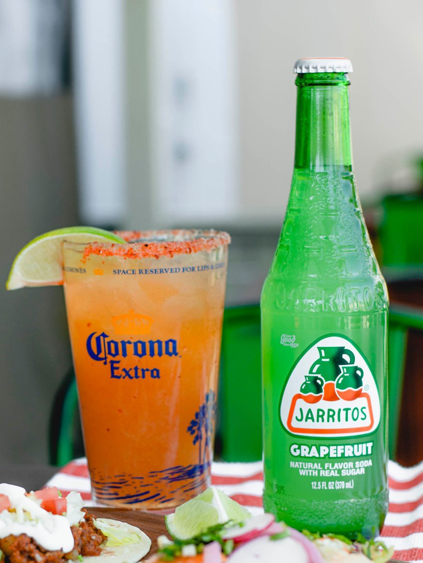 A bottle of jarritos grapefruit soda next to a glass of corona extra.