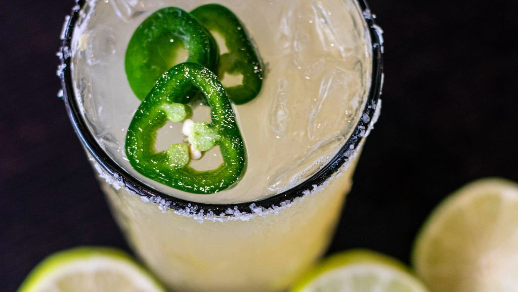 A close up of a margarita with jalapenos on top.