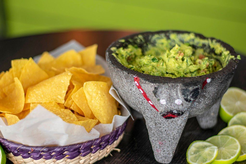 A bowl of guacamole next to a bowl of tortilla chips on a table.
