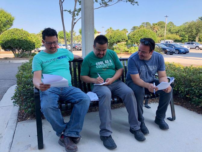 Three men are sitting on a bench with one wearing a green shirt that says you are a citizen