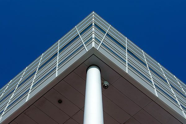 Low-angle view of modern building corner, blue sky background, white pillar supports roof.