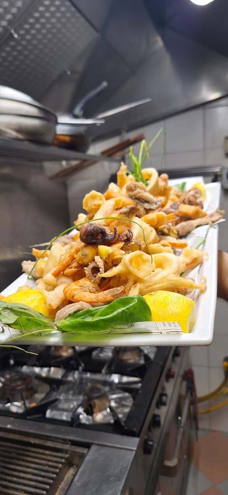 Piatto di pesce fritto con fette di limone nella cucina di un ristorante.