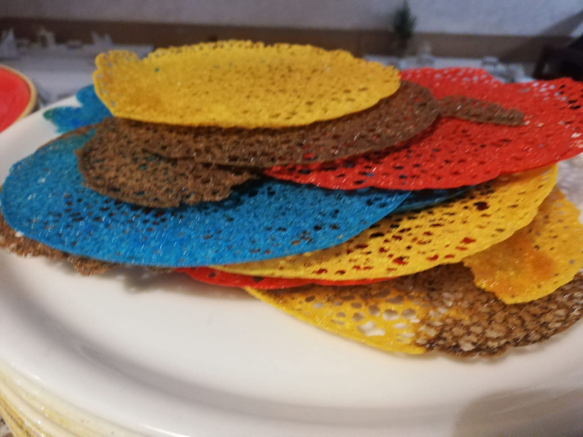 Cerchi colorati, sottili e ruvidi, impilati su un piatto bianco. Sfumature di blu, rosso, giallo e marrone.