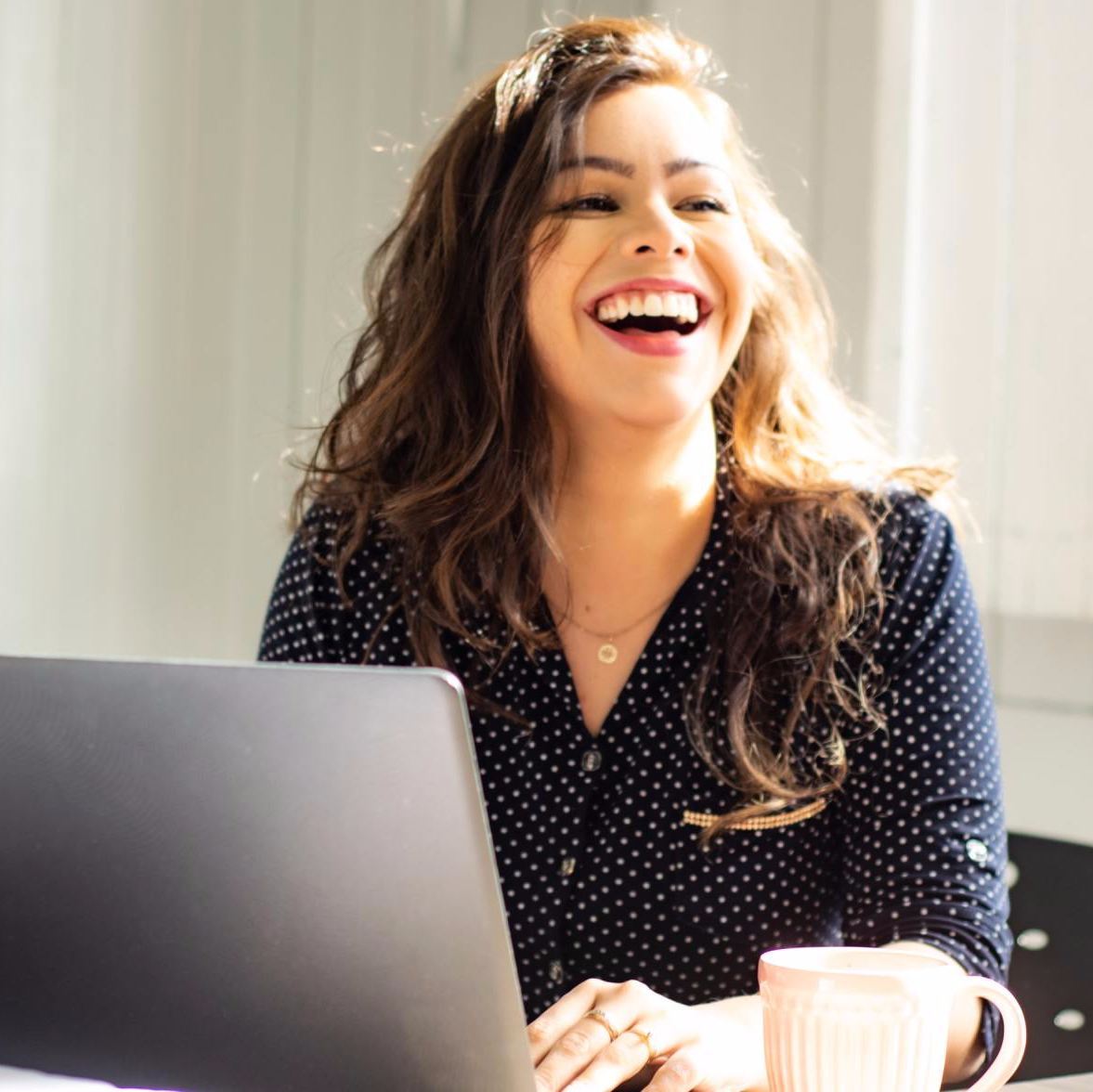 A woman is laughing while using a laptop computer