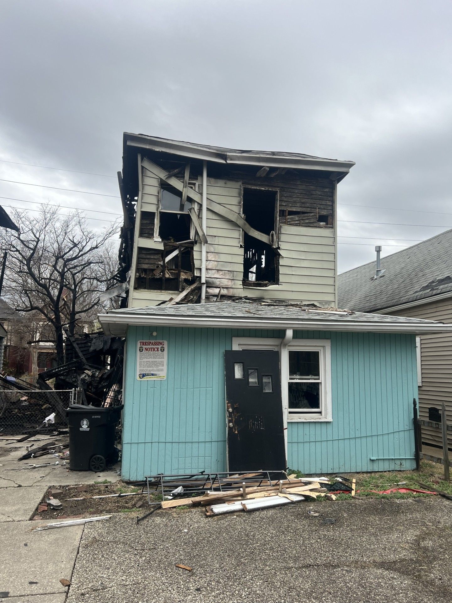 A severely fire-damaged two-story house with light blue siding on the bottom floor and exposed charred wood above.