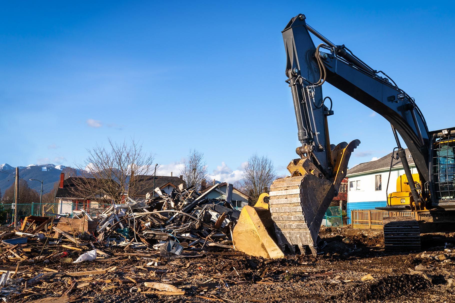 A large yellow excavator clears debris and piles of wreckage at a construction site against a clear blue sky. A large yellow excavator clears debris and piles of wreckage at a construction site against a clear blue sky.