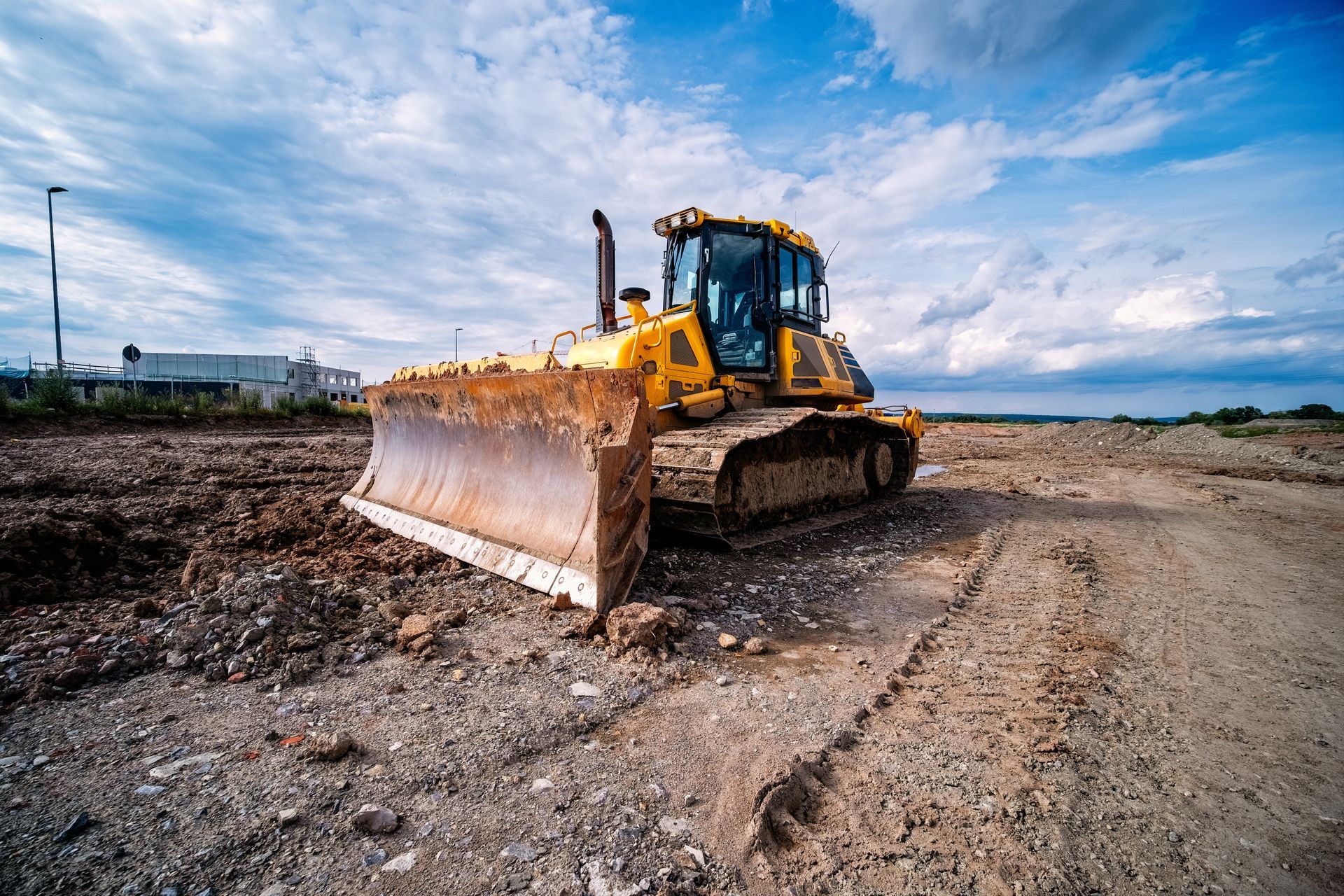 A yellow bulldozer sits on a rough, dirt construction site under a cloudy blue sky. A yellow bulldozer sits on a rough, dirt construction site under a cloudy blue sky.