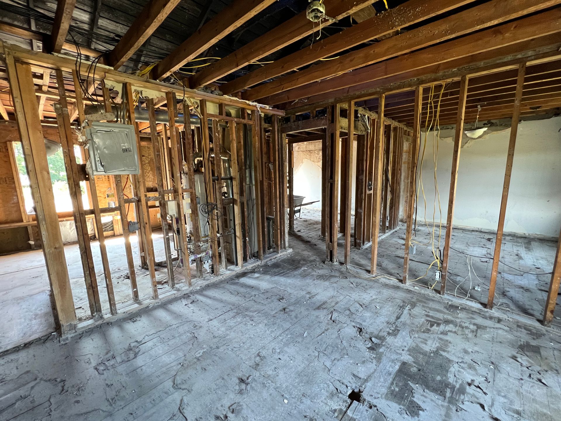 An unfinished interior room with exposed wooden wall studs, floor joists, and a bare concrete floor under construction.