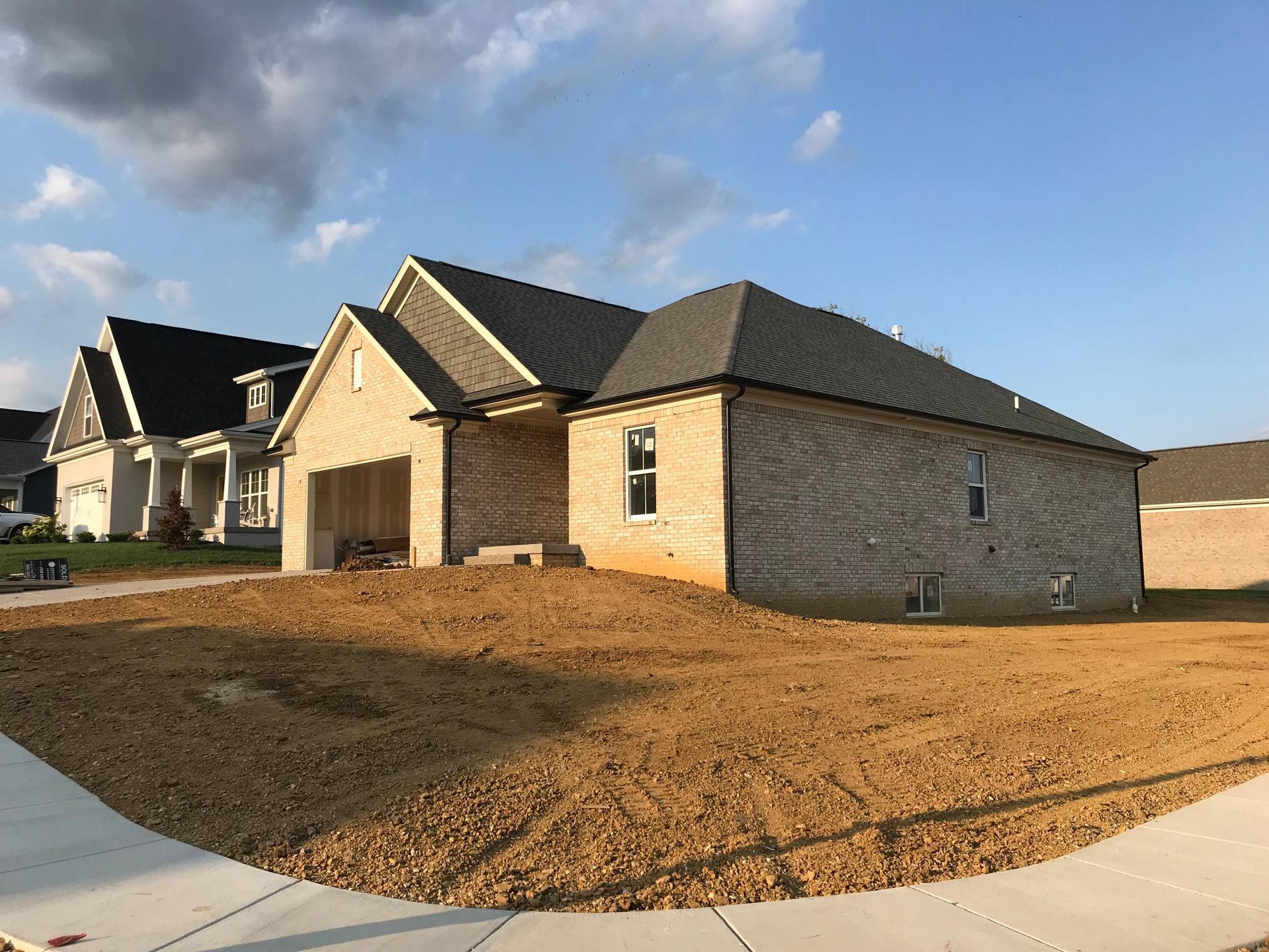 A newly constructed, light-colored brick house with a dark roof and unfinished yard, set next to another finished home. A newly constructed, light-colored brick house with a dark roof and unfinished yard, set next to another finished home.
