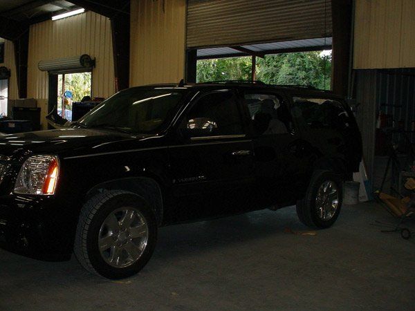 Black GMC Yukon SUV parked inside a garage with an open bay door.
