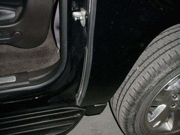 Black car door open, showing tire and interior, with black running board and weather stripping.