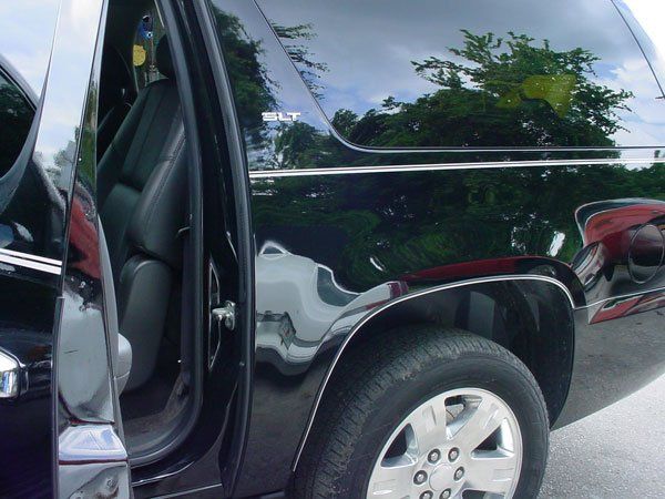 Black SUV with open door; reflecting sky, trees, and red vehicle.
