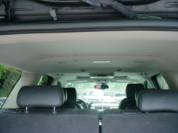 Interior view of a car with black seats and tan headliner; overhead console, windshield, and exterior visible.