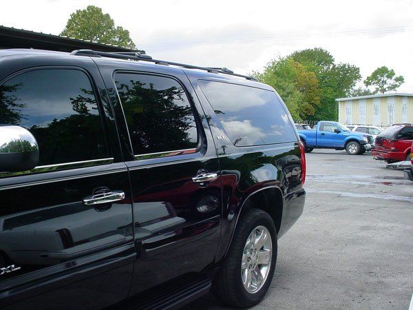 Black SUV parked in a lot with tinted windows, chrome accents, and a blue truck in the background.