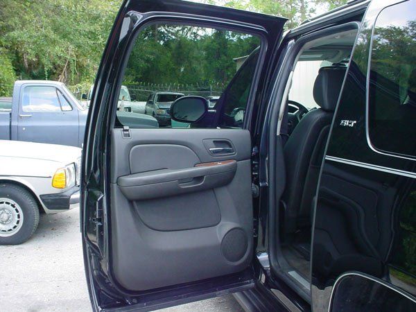 Black SUV door open, revealing interior details.  Other vehicles and trees are visible in the background.